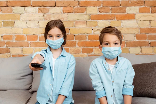 Selective focus of siblings in medical masks watching movie at home — Stock Photo