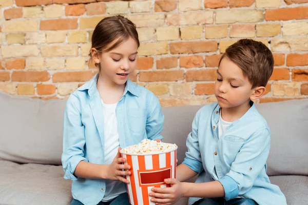 Siblings looking at tasty popcorn in bucket — Stock Photo