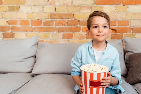 Lindo chico viendo película y sosteniendo palomitas de maíz cubo - foto de stock