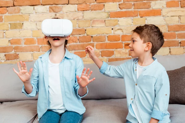 Щасливий брат дивиться на здивовану сестру в гарнітурі віртуальної реальності — стокове фото