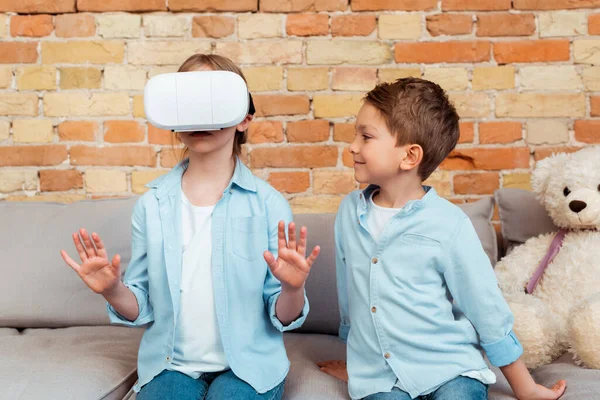 Happy brother looking at sister in virtual reality headset — Stock Photo