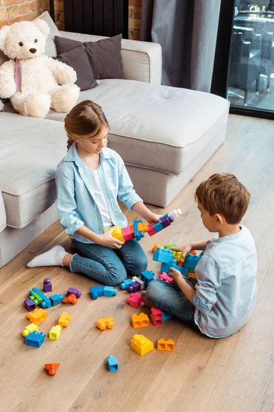 Hermanos jugando con bloques de construcción mientras están sentados en el suelo en la sala de estar - foto de stock