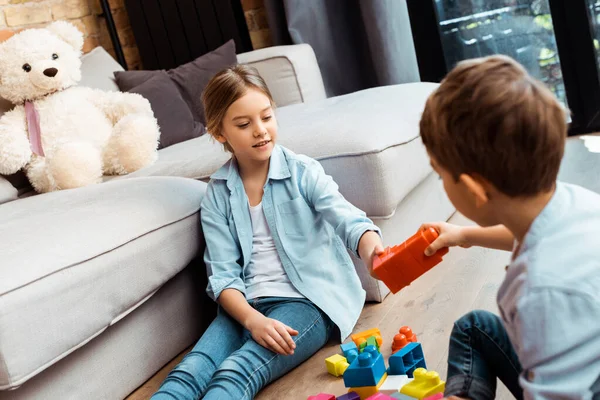 Selective focus of brother giving building block to sister at home — Stock Photo