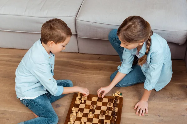 Overhead view of siblings playing chess on floor in living room — Stock Photo