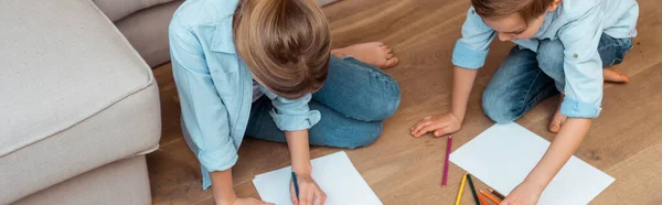 Panoramic crop of sister and brother sitting on floor and drawing in living room — Stock Photo