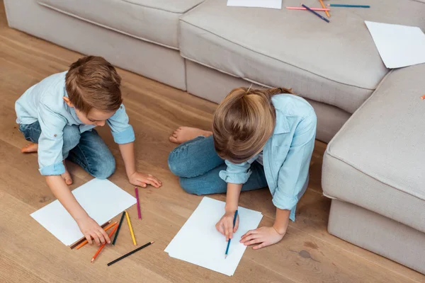 Hermana y hermano sentado en el suelo y dibujo en la sala de estar - foto de stock