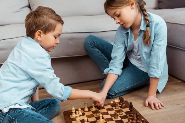 Mignons frères et sœurs jouant aux échecs sur le sol dans le salon — Photo de stock