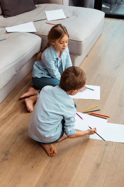 Cute sister and brother sitting on floor and drawing in living room — Stock Photo