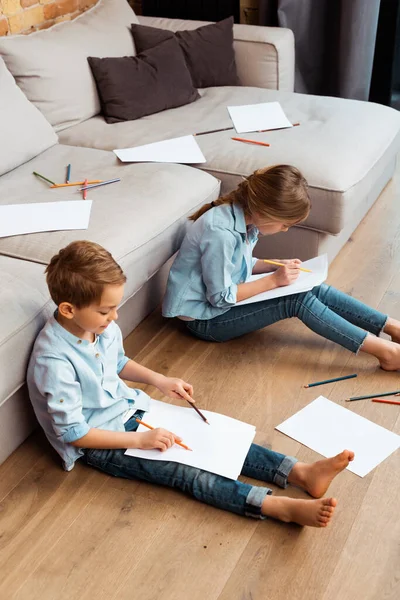 Lindo hermano y hermana sentado en el suelo y dibujo en la sala de estar - foto de stock