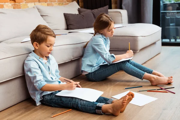 Nette Geschwister sitzen auf dem Boden und zeichnen im Wohnzimmer — Stockfoto