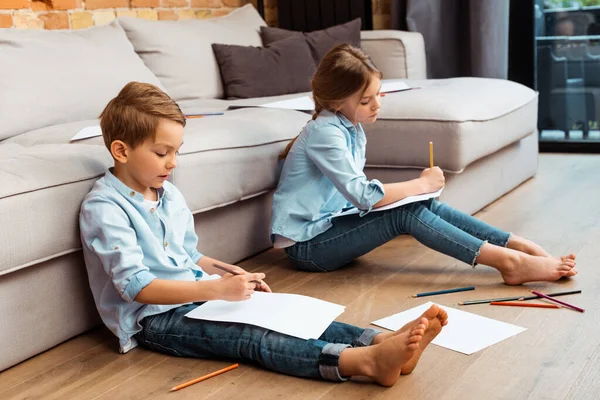 Frères et sœurs mignons assis sur le sol et le dessin dans le salon — Photo de stock