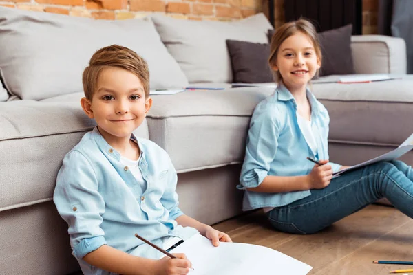 Selective focus of happy siblings drawing in living room — Stock Photo