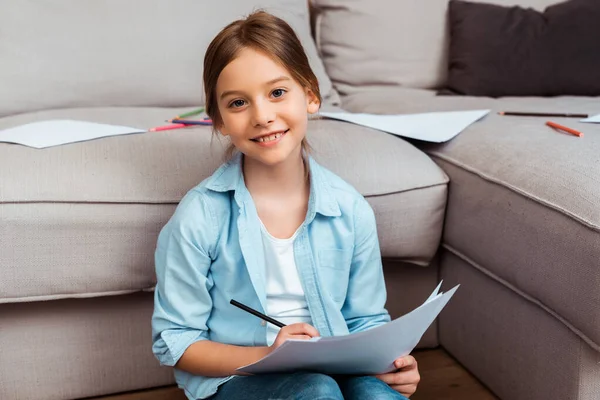 Lindo niño sonriendo mientras dibuja en la sala de estar - foto de stock