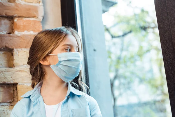 Kid in medical mask looking at window — Stock Photo