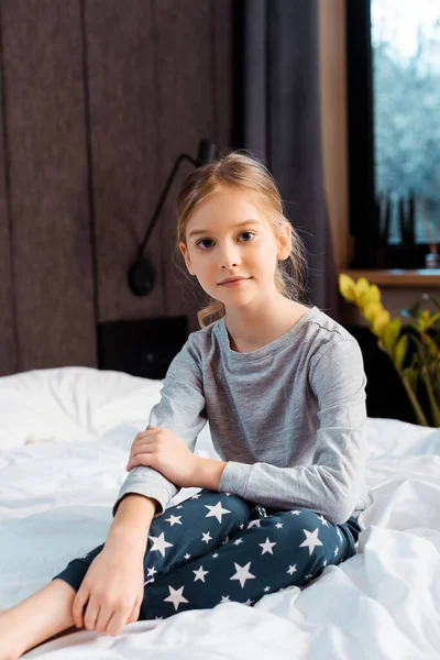 Bambino guardando la fotocamera e sorridendo seduto in camera da letto — Foto stock