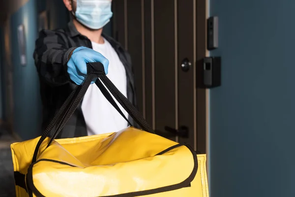 Selective focus of delivery man in medical mask and latex glove holding thermo bag in entryway — Stock Photo