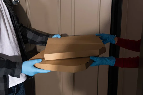 Cropped view of courier giving pizza boxes to woman in latex gloves near open door — Stock Photo