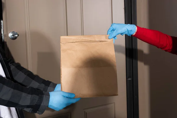 Ausgeschnittene Ansicht von Zusteller, der Frau Paket in Latexhandschuhen nahe geöffneter Tür übergibt — Stockfoto