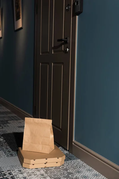 Пакет и коробки для пиццы на полу рядом с дверью в подъезде — стоковое фото