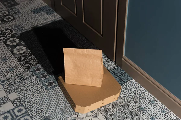 Vista de ángulo alto de cajas de pizza y paquete en el piso cerca de la puerta en la entrada - foto de stock