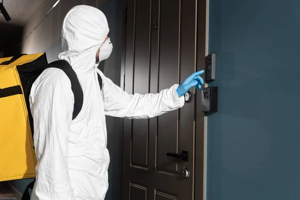 Side view of courier in hazmat suit, medical mask and latex glove ringing in doorbell — Stock Photo