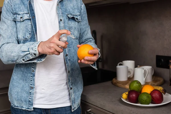 Cropped view of man using antiseptic for orange near fruits in kitchen — Stock Photo