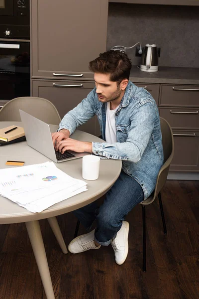 Télétravailleur utilisant un ordinateur portable près des documents et carte de crédit sur la table de cuisine — Photo de stock