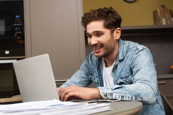 Selective focus of smiling teleworker using laptop in kitchen — Stock Photo