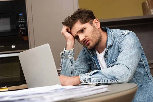 Focus selettivo dell'uomo sconvolto che guarda il laptop vicino ai documenti sul tavolo della cucina — Foto stock