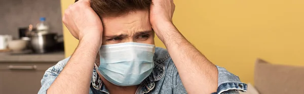 Panoramic crop of stressed man in medical mask looking away at home — Stock Photo