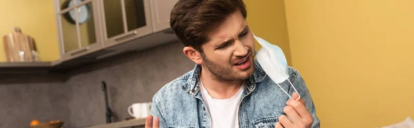 Panoramic orientation of confused man holding medical mask at home — Stock Photo