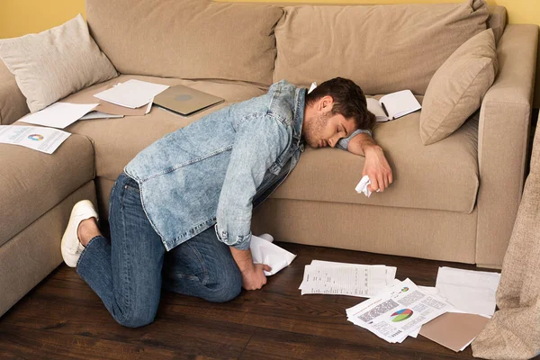 Side view of handsome man sleeping while holding clumped paper near laptop on couch — Stock Photo