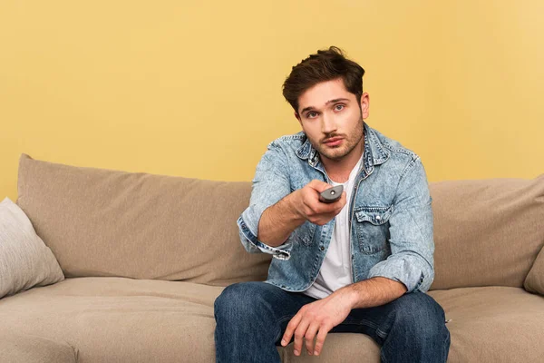 Beau homme tenant télécommande tout en étant assis sur le canapé — Photo de stock