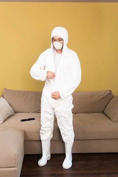 Young man in safety goggles and medical mask wearing hazmat suit at home — Stock Photo