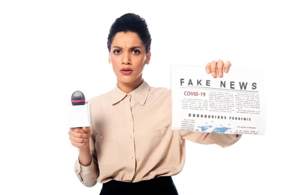 Worried african american journalist with microphone showing newspaper with fake news covid-19 text isolated on white — Stock Photo