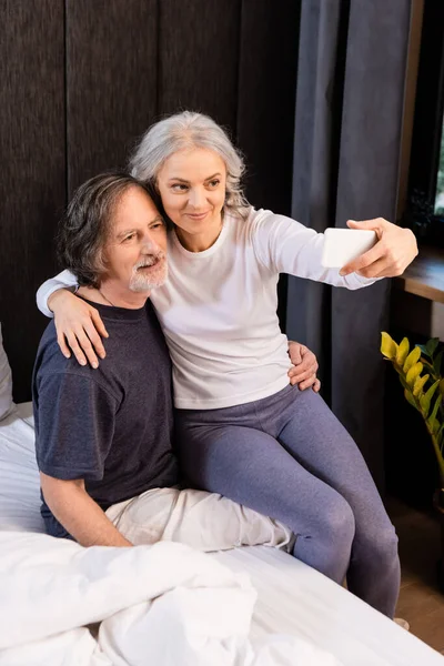 Mature woman taking selfie with husband in bedroom — Stock Photo