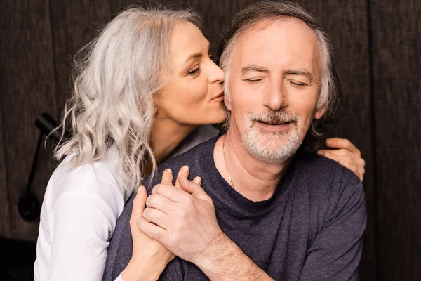 Reife Frau küsst Wange eines glücklichen Mannes mit geschlossenen Augen — Stockfoto