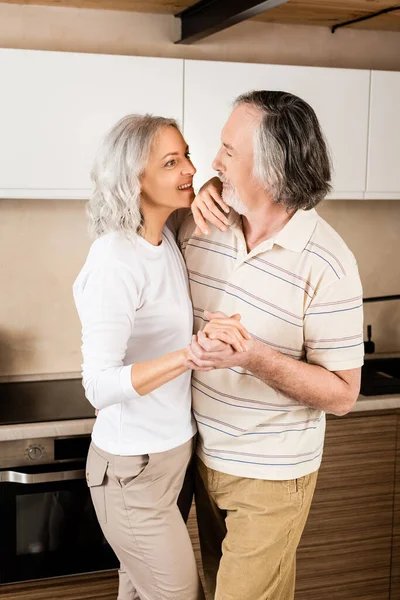 Happy mature couple holding hands while dancing in kitchen — Stock Photo