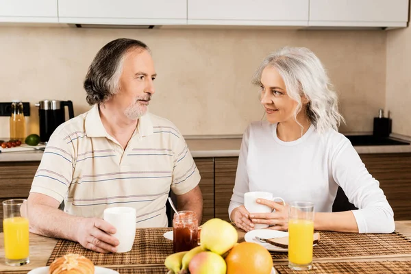 Glückliches reifes Paar schaut einander beim Frühstück auf dem Tisch an — Stockfoto