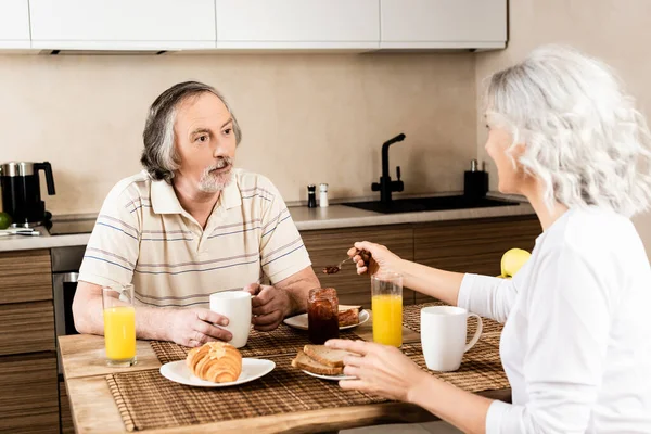 Selektiver Fokus des bärtigen und reifen Mannes, der seine Frau in der Nähe des leckeren Frühstücks anschaut — Stockfoto