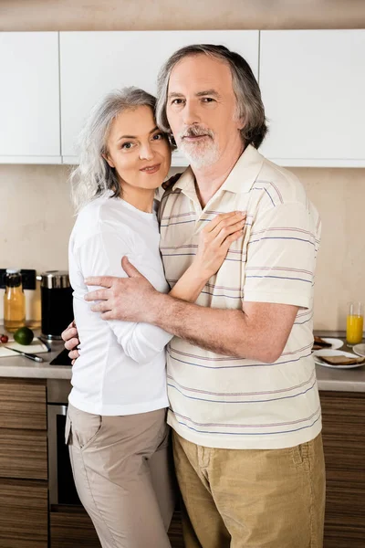 Feliz pareja de mediana edad abrazándose en la cocina - foto de stock