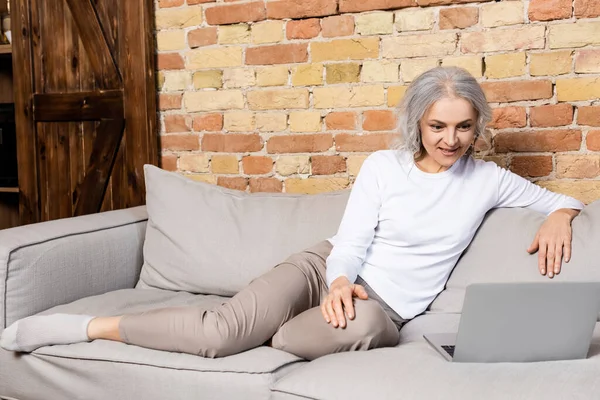 Весела і зріла жінка дивиться фільм на ноутбук у вітальні — стокове фото