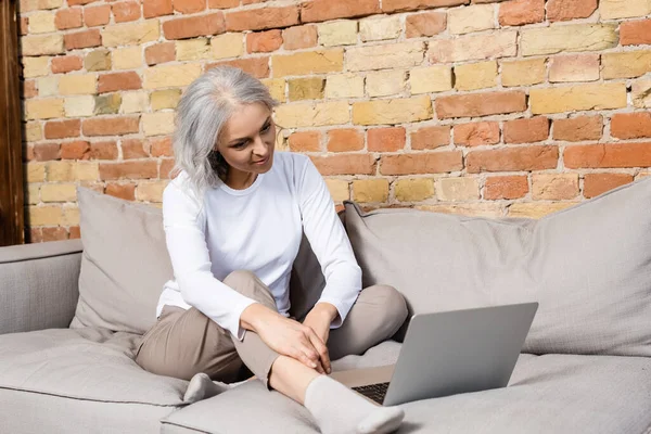 Happy and mature woman watching movie on laptop in living room — Stock Photo