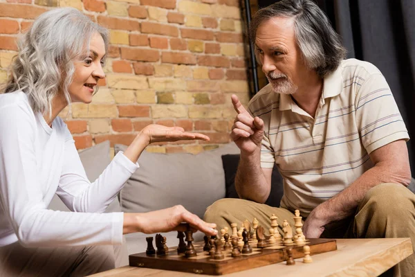 Mature husband and wife playing chess in living room — Stock Photo