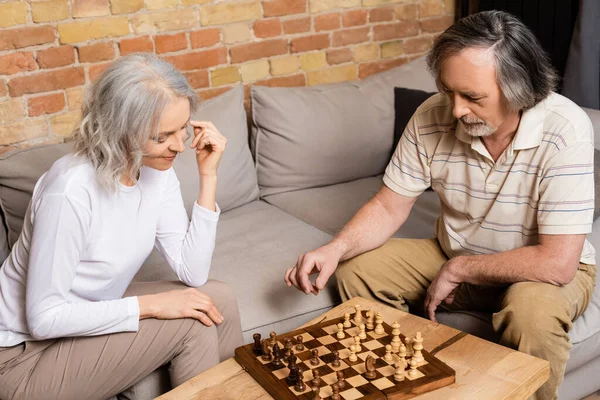 Mature man and woman playing chess in living room — Stock Photo