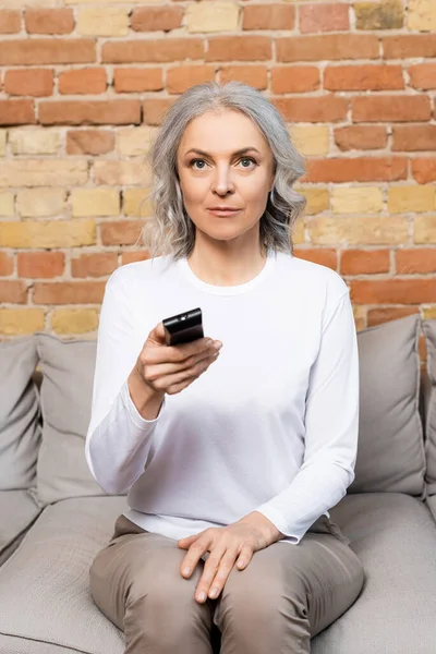 Mature woman holding remote controller while watching movie at home — Stock Photo
