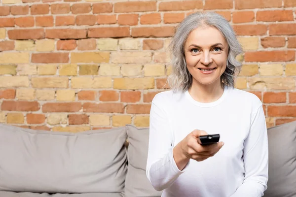 Happy and mature woman holding remote controller while watching movie at home — Stock Photo