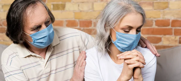 Горизонтальный урожай зрелого мужчины в медицинской маске трогательной жены с сжатыми руками — стоковое фото