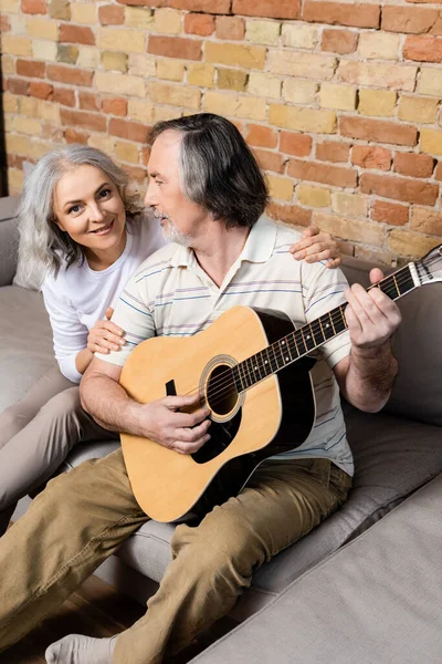 Bärtiger und reifer Mann spielt Akustikgitarre neben fröhlicher Frau — Stockfoto