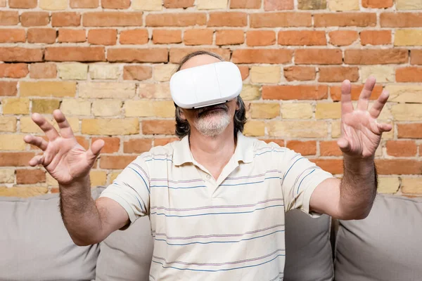 Mature man in virtual reality headset gesturing at home — Stock Photo